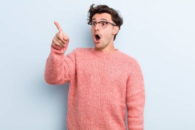 Genç yakışıklı adam şaşkın ve şaşırmış hissediyor, hayranlıkla yukarı bakıyor, şaşırmış, ağzı açık bakıyor.