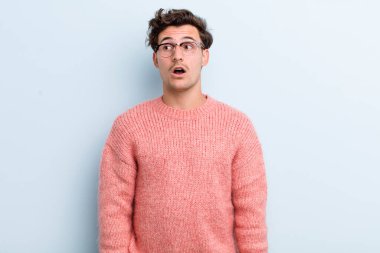 Genç yakışıklı adam şok olmuş, mutlu, şaşkın ve şaşırmış hissediyor, ağzı açık bir şekilde yana bakıyor.