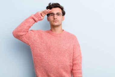 Genç ve yakışıklı bir adam saygı göstererek, onur ve vatanseverlik adına askeri bir selamla kamerayı selamlıyor.