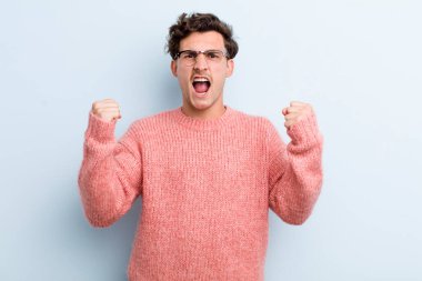 Genç yakışıklı bir adam sinirli bir ifadeyle ya da yumruklarıyla başarıyı kutlarken agresif bir şekilde bağırıyor.