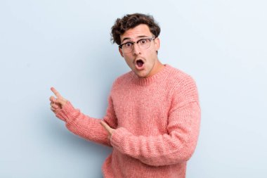 Genç yakışıklı adam şaşkın ve şaşırmış hissediyor. Kenardaki fotokopi alanını işaret ediyor. Şaşırmış, ağzı açık bir bakış.