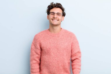 Genç ve yakışıklı bir adam neşeli, neşeli, mutlu, kendinden emin ve rahat bir ifadeyle gülümsüyor.