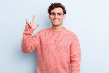 Genç yakışıklı adam kendini mutlu, eğlenceli, kendinden emin, pozitif ve asi hissediyor, elle rock ya da heavy metal işareti yapıyor.