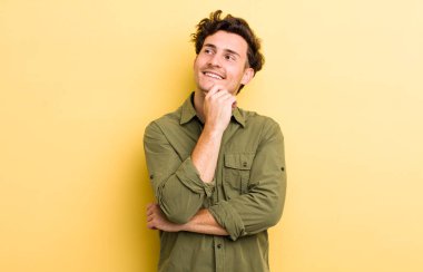 Genç yakışıklı adam mutlu bir şekilde gülümsüyor ve hayal kuruyor ya da şüphe ediyor.