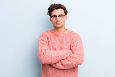 Genç yakışıklı adam hayal kırıklığına uğramış ve hayal kırıklığına uğramış, ciddi görünüyor, kızgın ve kollarını kavuşturmuş.