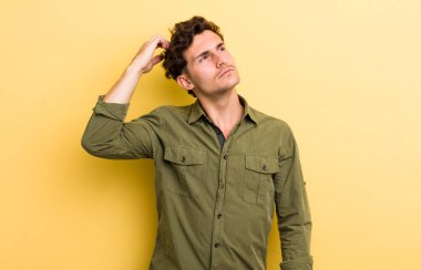 Genç yakışıklı adam şaşkın ve şaşkın hissediyor, başını kaşıyor ve yana bakıyor.