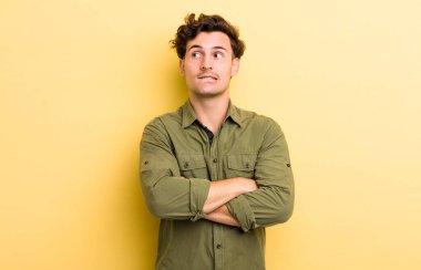 Genç yakışıklı adam şüphe ediyor ya da düşünüyor, dudağını ısırıyor ve kendini güvensiz ve gergin hissediyor, kenarda yer arıyor.