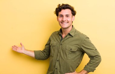 Genç yakışıklı adam kendini mutlu ve neşeli hissediyor, gülümsüyor ve seni selamlıyor, dostça bir jestle içeri davet ediyor.