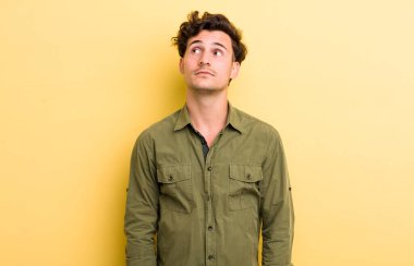 Endişeli, kafası karışık, budala bir ifadeyle genç yakışıklı adam, kopya alanı arıyor, şüphe ediyor.