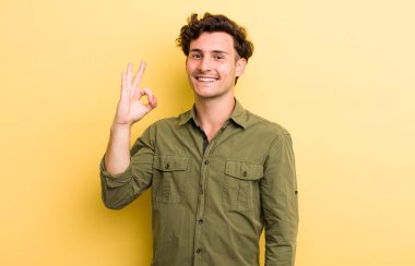 Genç yakışıklı adam mutlu, rahat ve tatmin olmuş hissediyor. Onayını iyi bir hareketle gösteriyor. Gülümsüyor.