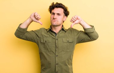 Genç yakışıklı adam üzgün, hayal kırıklığına uğramış ya da kızgın görünüyor, anlaşmazlık içinde baş parmağını gösteriyor, hayal kırıklığına uğramış hissediyor.