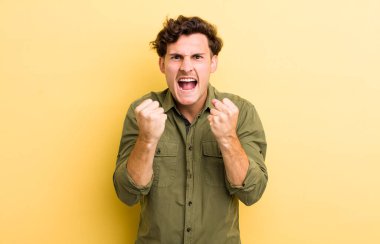 Genç yakışıklı adam sinirli, sinirli, sinirli bakışlar ve sıkı yumruklar ile agresif bir şekilde bağırıyor.