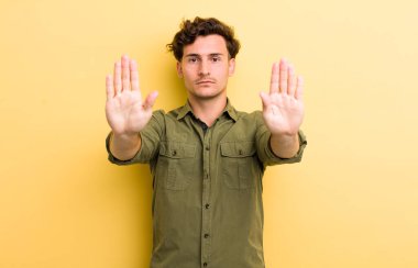 Genç yakışıklı adam ciddi, mutsuz, kızgın ve hoşnutsuz görünüyor. Ya da her iki avuçta da dur diyor.