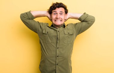 Genç ve yakışıklı bir adam stresli, endişeli, endişeli ya da korkmuş, elleri başının üstünde, hata yaptığında panikliyor.