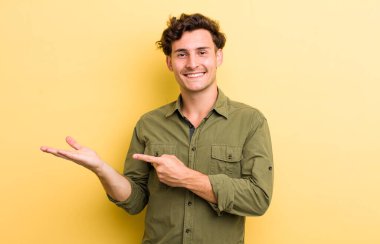 Genç yakışıklı adam gülümsüyor, mutlu, tasasız ve tatmin olmuş hissediyor, fotokopi alanındaki konsepte ya da fikre işaret ediyor.