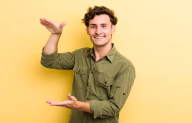 Genç yakışıklı adam gülümsüyor, mutlu, pozitif ve tatmin olmuş hissediyor, fotokopi alanında nesne ya da konsept tutuyor ya da gösteriyor