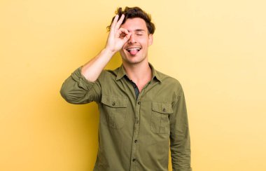 Genç yakışıklı adam mutlu bir şekilde gülümsüyor, şaka yapıyor ve gözetleme deliğinden bakıyor, sırları gözetliyor.