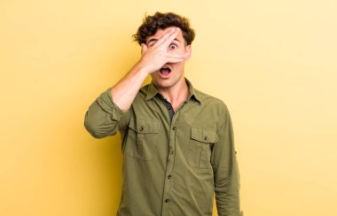 Genç yakışıklı adam şok olmuş, korkmuş ya da korkmuş görünüyor. Yüzü elle kaplanmış ve parmaklarının arasından gizlice bakıyor.