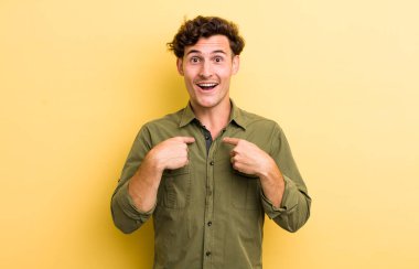 Genç yakışıklı adam mutlu, şaşkın ve gururlu, heyecanlı, şaşkın bakışlarıyla kendini işaret ediyor.
