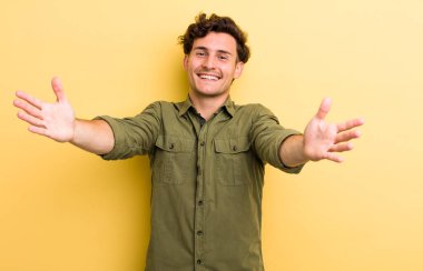 Genç yakışıklı adam neşeyle gülümsüyor sıcak, dostça, sevgi dolu bir kucak veriyor, mutlu ve sevimli hissediyor.