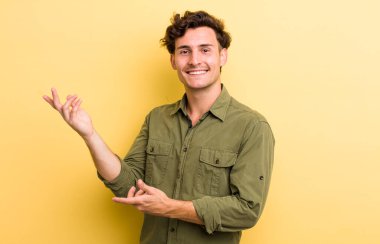 Genç yakışıklı adam gururla ve kendinden emin bir şekilde gülümsüyor, mutlu ve tatmin olmuş hissediyor ve fotokopi alanında bir konsept gösteriyor.