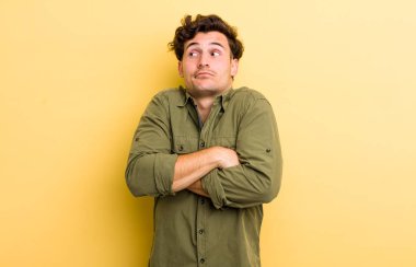 Genç yakışıklı adam omuz silkiyor, kafası karışık ve kararsız, kolları bağlı ve şaşkın görünüyor.