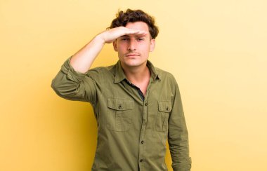 Genç yakışıklı adam şaşkın ve şaşkın bakıyor, el üstünde uzak bakıyor, izliyor ya da arıyor