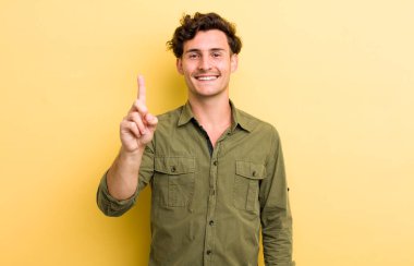 Genç yakışıklı adam gülümsüyor ve arkadaş canlısı görünüyor, bir numara ya da ilk eli önde, geriye doğru sayıyor.