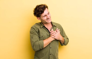 Genç yakışıklı adam üzgün, yaralı ve kalbi kırık görünüyor, iki elini de kalbine yakın tutuyor, ağlıyor ve bunalımda.