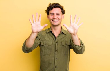 Genç yakışıklı adam gülümsüyor ve arkadaş canlısı görünüyor, onuncu veya onuncu numarayı gösteriyor, eli önde, geriye doğru sayıyor.