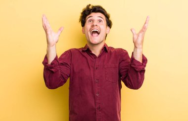 Genç yakışıklı adam kendini mutlu, şaşkın, şanslı ve şaşırmış hissediyor. Zaferi kutlarken iki elini de havaya kaldırıyor.