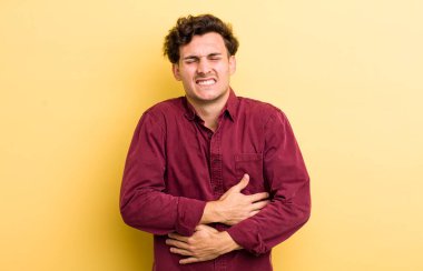 Genç ve yakışıklı bir adam endişeli, hasta, hasta ve mutsuz hissediyor. Ağrılı bir mide ağrısı ya da grip geçiriyor.