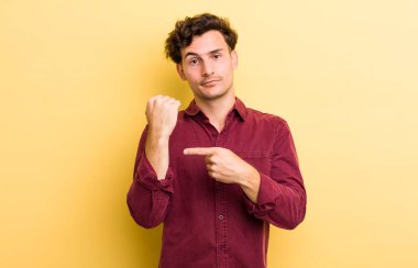 Genç yakışıklı adam sabırsız ve kızgın görünüyor, saati gösteriyor, dakiklik istiyor, zamanında gelmek istiyor.