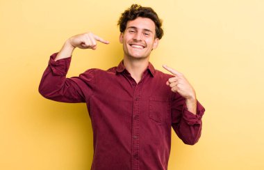 Genç yakışıklı adam, kendine güvenerek gülümsüyor. Geniş bir gülümseme, pozitif, rahat, tatmin olmuş bir tavır.