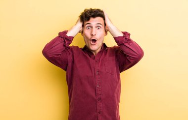 Genç yakışıklı adam heyecanlı ve şaşırmış görünüyor, ağzı açık, elleri başının üstünde, şanslı bir kazanan gibi hissediyor.