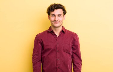 Genç yakışıklı adam pozitif ve kendinden emin gülümsüyor. Tatmin olmuş, arkadaş canlısı ve mutlu görünüyor.