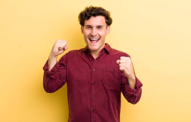 Genç yakışıklı adam mutlu, şaşırmış ve gururlu, bağırıyor ve başarıyı büyük bir gülümsemeyle kutluyor.