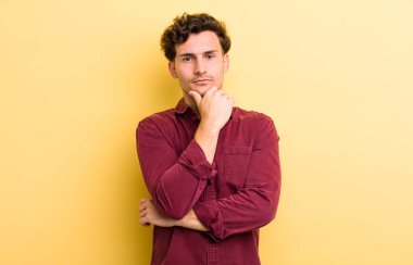 Genç yakışıklı adam ciddi görünüyor, kafası karışık, kararsız ve düşünceli, seçenekler ve seçimler arasında şüpheci.