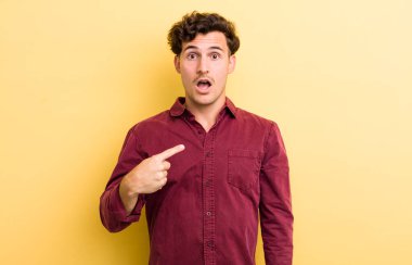 Şok olmuş ve ağzı açık, kendini işaret eden genç yakışıklı bir adam.
