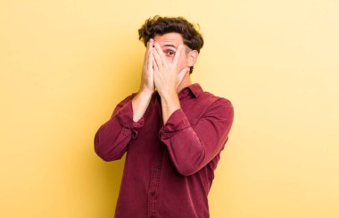 Genç ve yakışıklı bir adam korkmuş ya da utanmış hissediyor. Gözleri yarı kapalı ya da ellerle dikizliyor ya da dikizliyor.