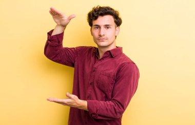 Genç yakışıklı bir adam iki eli de yan tarafında fotokopi alanı olan bir nesneyi tutuyor, bir nesneyi gösteriyor, sunuyor ya da reklamını yapıyor.