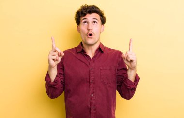 Genç ve yakışıklı bir adam şaşkınlık ve şaşkınlık dolu bakışlarla yukarıyı işaret ederek huşu içinde ve açık ağızlı hissediyor.