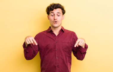 İki eliyle aşağıya bakan ağzı açık genç yakışıklı adam, şaşkın, şaşkın ve şaşırmış görünüyor.