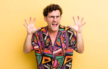 Genç ve yakışıklı bir adam panik ya da öfke içinde bağırıyor, şok olmuş, korkmuş ya da öfkeli, elleri başının yanında.