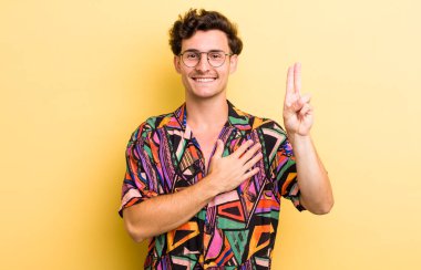 Genç yakışıklı adam mutlu, kendinden emin ve güvenilir görünüyor, gülümsüyor ve zafer işareti gösteriyor, olumlu bir tavırla.