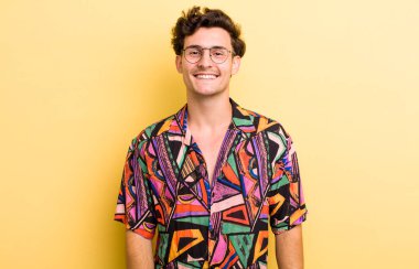 Genç ve yakışıklı bir adam neşeli, neşeli, mutlu, kendinden emin ve rahat bir ifadeyle gülümsüyor.