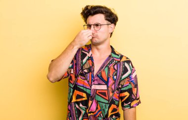 Genç yakışıklı adam iğreniyor, kötü ve nahoş bir koku duymamak için burnunu tutuyor.