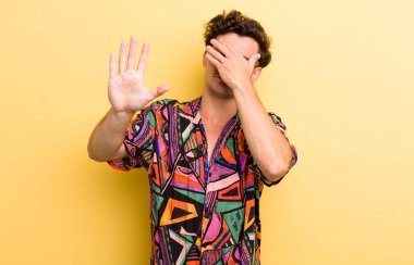 Genç ve yakışıklı bir adam elleriyle yüzünü kapatıyor ve kamerayı durdurmak için diğer elini öne koyuyor. Fotoğraf ya da resimleri reddediyor.