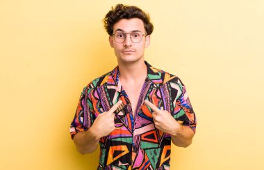 Genç ve yakışıklı bir adam kendini işaret ediyor. Şaşırmış ve şaşırmış bir şekilde bakıyor.
