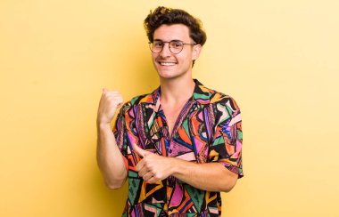 Genç yakışıklı adam neşeyle gülümsüyor ve yan taraftaki fotokopi alanını gösteriyor, mutlu ve tatmin olmuş hissediyor.